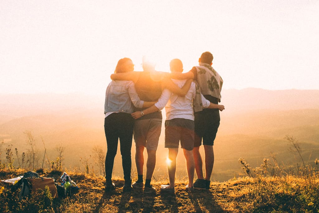 Grupo de amigos abraçados no alto de uma serra, olhando o nascer do sol